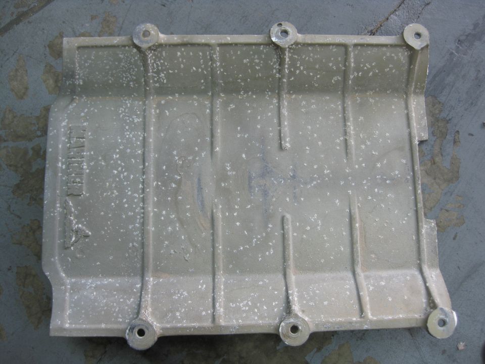 Aluminum part with bolt holes and ribbed surface. Text visible on left