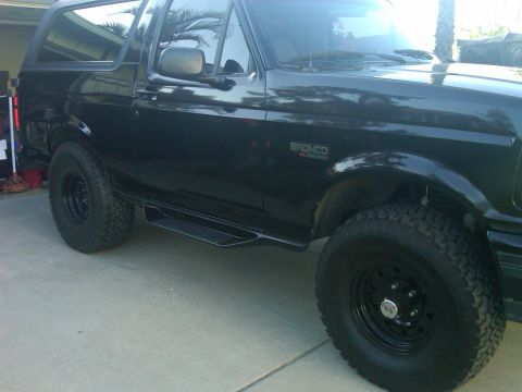 1986 Ford Bronco - A black Ford Bronco is parked on a concrete surface, viewed from the side.