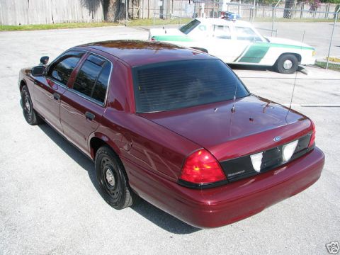 2005 Ford Crown Victoria - Maroon 2005 Ford Crown Victoria, rear 3/4 view, with another police car in the background.