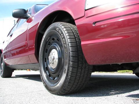 2005 Ford Crown Victoria - The side profile of a red sedan is captured, focusing on the front wheel and tire assembly.