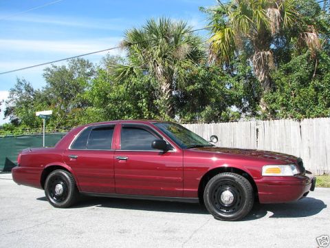 2005 Ford Crown Victoria - This red 2005 Ford Crown Victoria sedan is viewed from the front three-quarter angle, showing its tinted windows and black steel wheels.