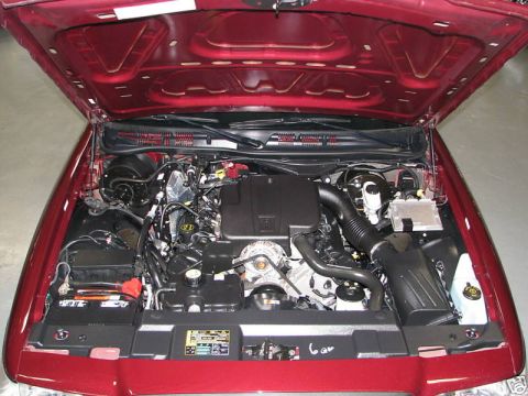 2005 Ford Crown Victoria - The engine bay of a red 2005 Ford Crown Victoria is visible with the hood raised, revealing the V8 engine and associated parts.