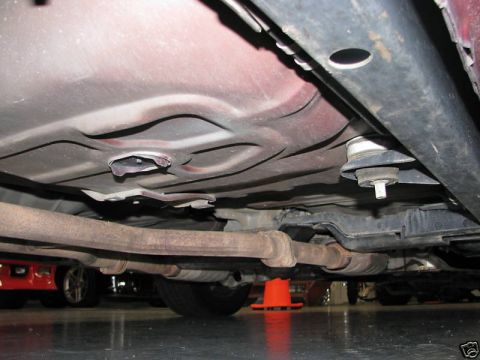 2005 Ford Crown Victoria - The undercarriage of a vehicle is shown, with focus on the exhaust system and frame components. A red car is visible in the background.