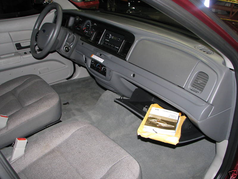 2005 Ford Crown Victoria interior, showing dashboard, steering wheel, and seats. Owner's manual visible in glove compartment