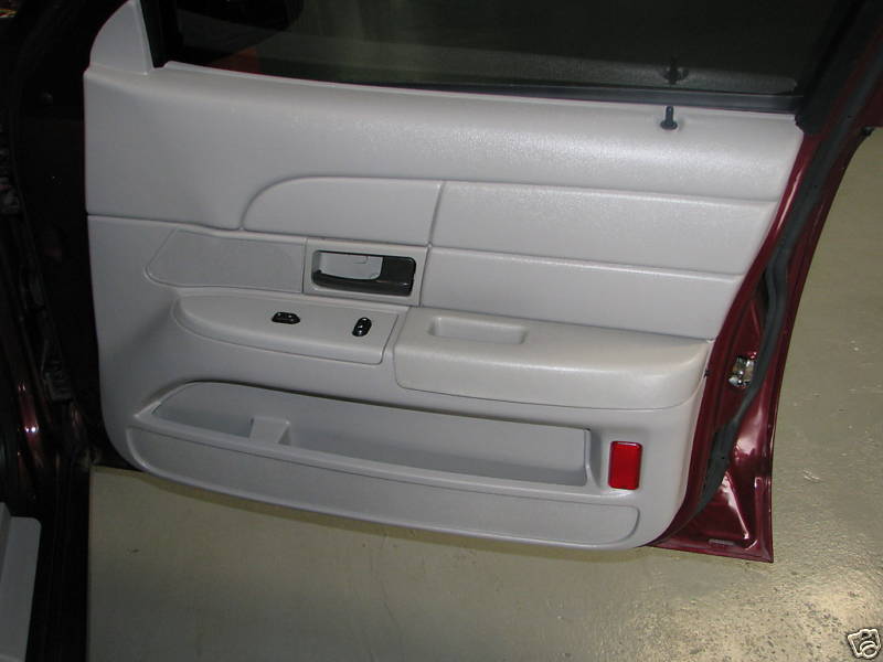 Interior of a car door with light gray paneling, black door handle, and window controls