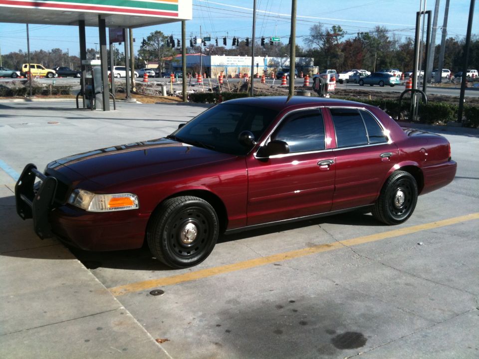 Maroon 2005 Ford Crown Victoria with push bumper parked at a gas station