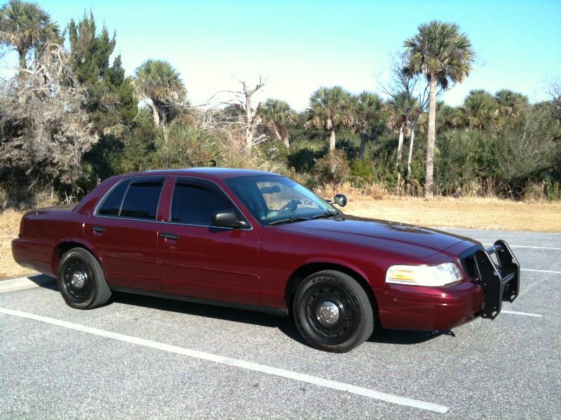 Maroon 2005 Ford Crown Victoria Police Interceptor parked in a lot with trees and sky in background