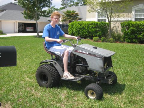 2006 Honda RANCHER - Teenager rides a Craftsman lawn tractor on a sunny day in a suburban yard.