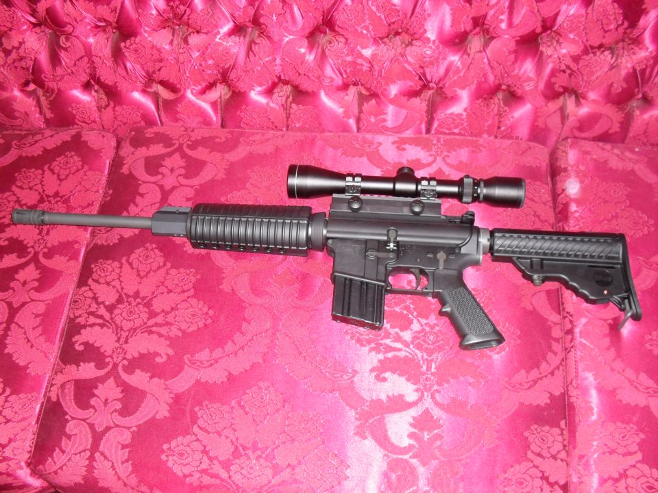 AR-style rifle with scope lying on a pink fabric surface