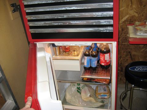 1999 Ford Crown Victoria - A red refrigerator is filled with various drinks and food items, with a toolbox mounted above it.