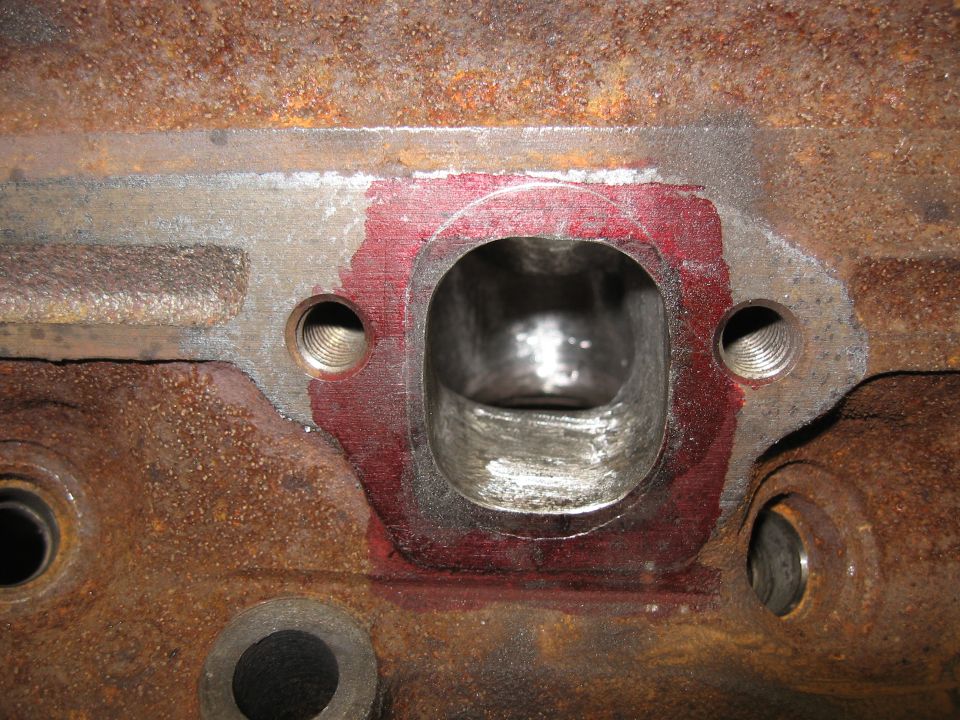 Close-up of a rusty engine block with a port that has red sealant around it