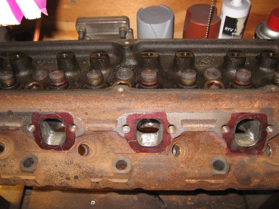 Rusty engine cylinder head with red gasket material around exhaust ports