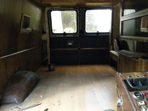 1981 Ford E350 - The interior of a van shows wood paneling, rear doors, and a bench seat, with the floor appearing worn.