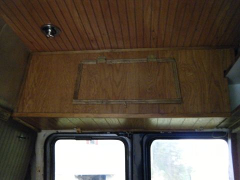 1981 Ford E350 - The interior of a van shows wood paneling on the ceiling and walls, with an overhead storage unit.