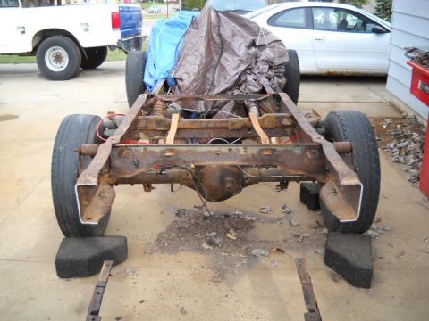 1954 Ford F-100 - A heavily rusted truck chassis sits on blocks, partially covered by a tarp, with other vehicles nearby.
