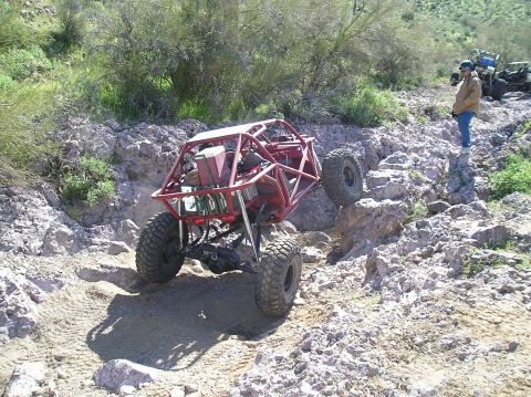 1986 Toyota Hilux - A red tube-frame rock buggy with an open roll cage, front-mounted winch and mud-terrain tires climbing out of a rocky desert gully, rear wh…