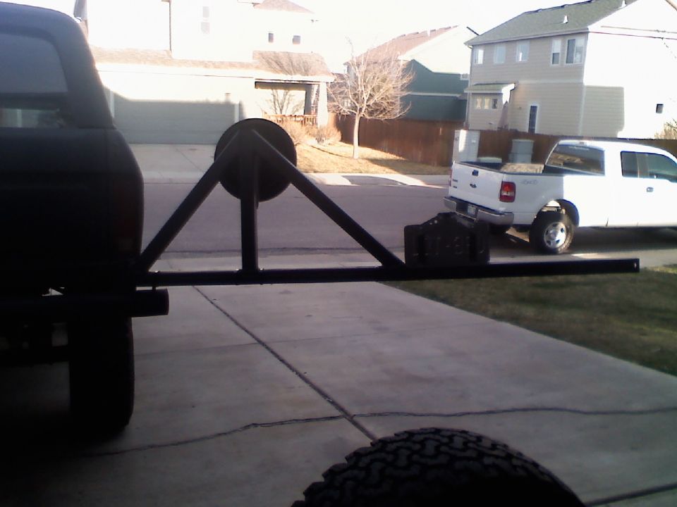 Rear tire carrier on dark SUV, with a white pickup truck in the background