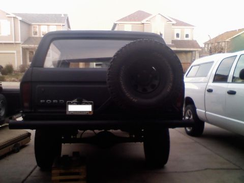 1979 Ford Bronco - Black Ford Bronco with spare tire and custom bumper, parked next to a white pickup truck.