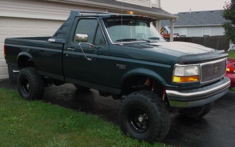 1995 Ford F-150 - A dark green Ford F-150 truck is parked in front of a garage with a modified cab roof.