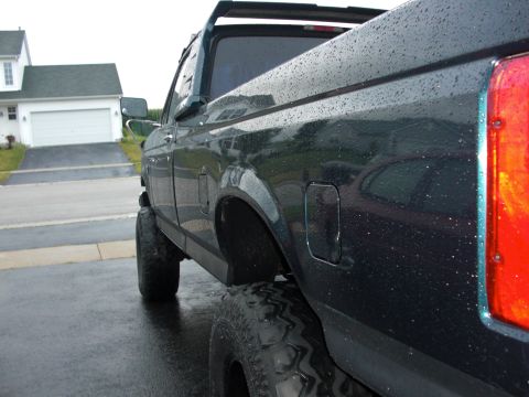 1995 Ford F-150 - Pickup truck with large tires parked on a wet road, side view.