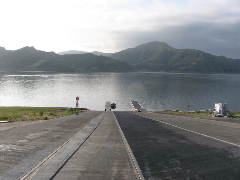 Concrete boat launch ramp leading into a reservoir surrounded by green hills