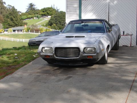 1973 Ford Ranchero - A silver 1972 Ford Ranchero is parked in front of a building, with a grassy hill and houses in the background.