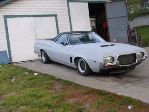 1973 Ford Ranchero - This 1972 Ford Ranchero is primer gray and has a black vinyl roof, parked outside a garage.