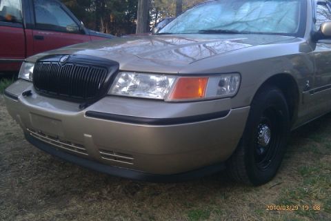 2000 Mercury Grand Marquis - The front end of a gold Mercury Grand Marquis is visible, parked next to a red truck.