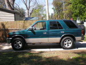 1993 Isuzu Rodeo - Side view of a green SUV parked next to a house, a spare tire mounted on the rear door.