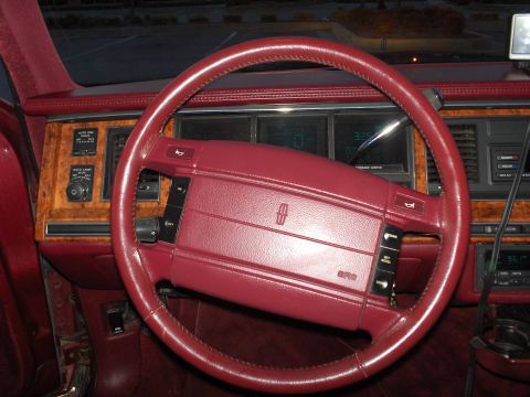 1993 Lincoln Town Car - The interior of a 1990s Lincoln Town Car, a red steering wheel and wood-grain dashboard accents.
