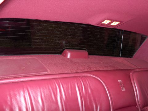 1993 Lincoln Town Car - The plush red interior of a 1993 Lincoln Town Car, its rear seating area and window.
