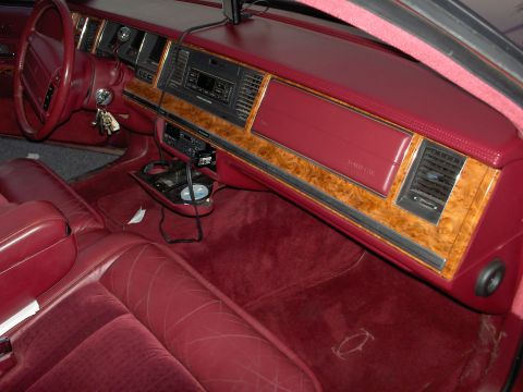 1993 Lincoln Town Car - The interior of a red car features wood grain trim on the dashboard and seats with a diamond pattern.