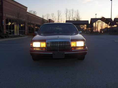 1993 Lincoln Town Car - The front of a red 1993 Lincoln Town Car is shown with its headlights on at dusk.