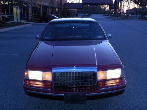 1993 Lincoln Town Car - A red sedan is parked in a lot at dusk, showing its front grille and headlights.