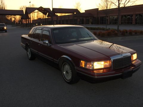 1993 Lincoln Town Car - A maroon 1993 Lincoln Town Car is parked in a lot as the sun sets, with another vehicle visible in the distance.