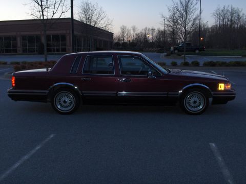1993 Lincoln Town Car - A maroon sedan is parked in a lot at dusk, showing its side profile and chrome accents.
