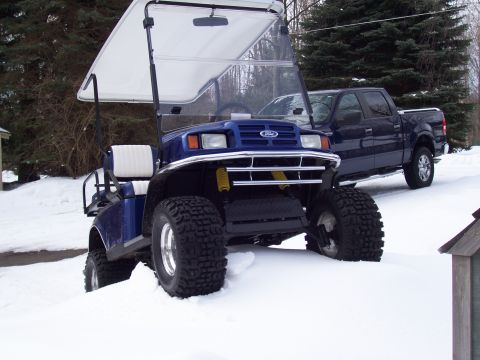 1978 Ford F-150 - A blue golf cart with oversized tires sits in the snow, with a dark blue pickup truck parked behind it.