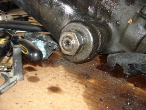 1992 Ford Bronco - Close-up of a greasy mechanical component, likely from a vehicle, with a prominent bolt and oil spills on a wooden surface.