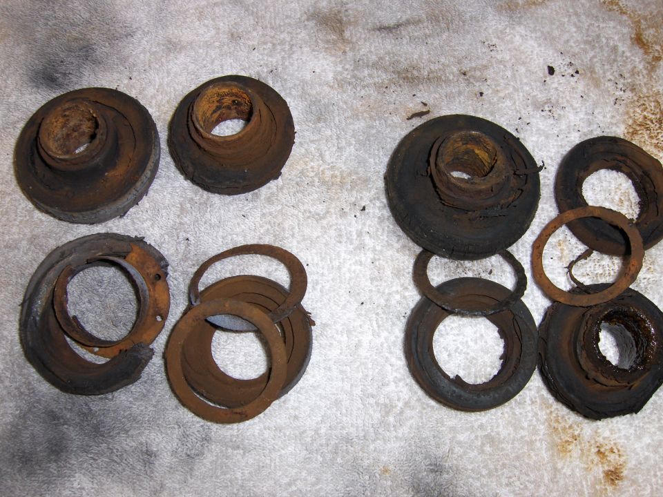 Several rusty, worn suspension bushings and metal rings laid out on a textured surface