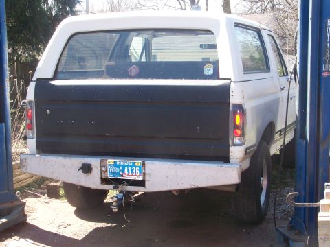 1989 Ford Bronco - Rear view of a white full-size Dodge SUV/truck raised on a two-post shop lift, with a black lower tailgate panel, Indiana plate and a ball-…