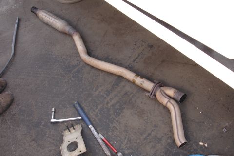 1989 Ford Taurus - An exhaust pipe is shown on the ground, with a Y-shaped connector and various tools nearby.