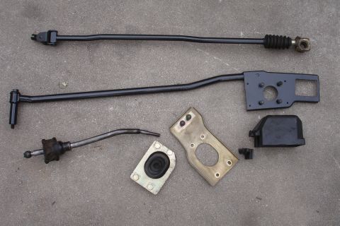 1989 Ford Taurus - Several metal and rubber components for a car's manual shifter system are displayed on a rough surface.
