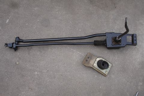 1989 Ford Taurus - A disassembled rod shifter assembly and its mounting bracket lie on a concrete surface.