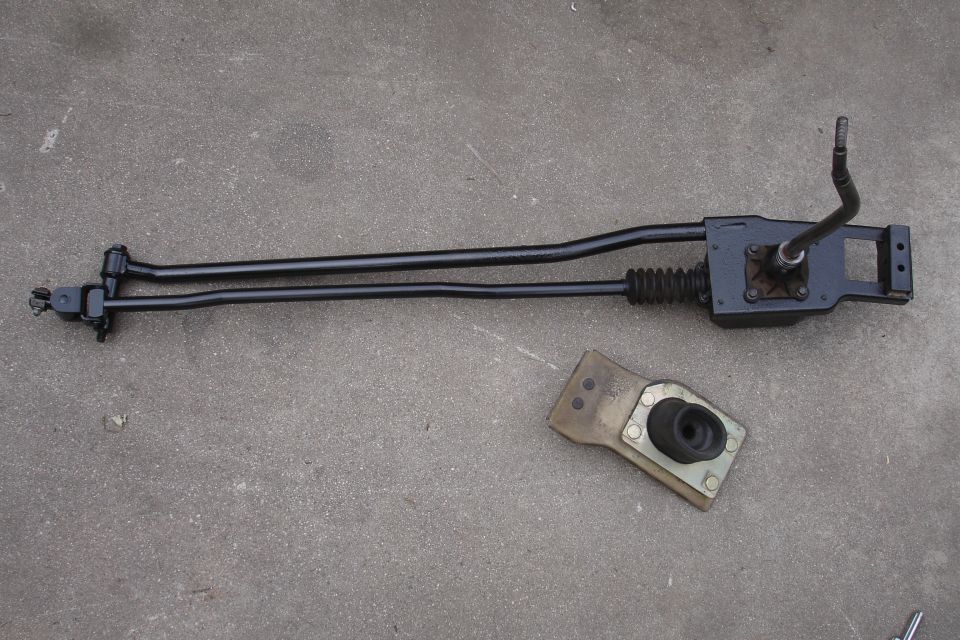 Rod shifter assembly with two black rods and a black shifter lever, next to a metal bracket with a rubber boot