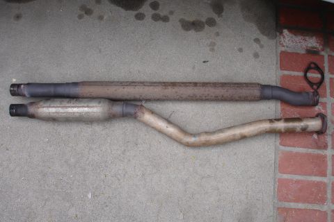 1989 Ford Taurus - Two exhaust pipes, one straight and one curved, are shown laid out on a concrete surface.
