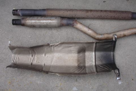 1989 Ford Taurus - Exhaust system components, including pipes and a heat shield, laid out on a concrete surface.