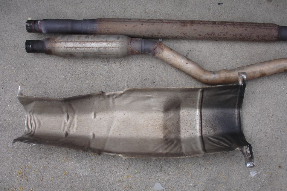 Two sections of exhaust pipe and a damaged heat shield on concrete