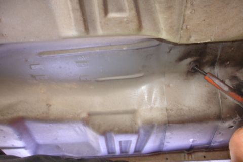 1989 Ford Taurus - Close-up view of the undercarriage of a vehicle, revealing structural details and a tool in use.