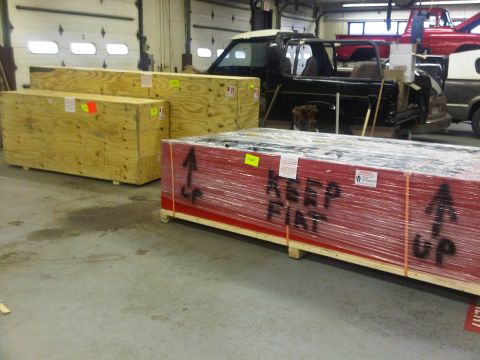1996 Ford Bronco - A disassembled black SUV sits in a garage next to wooden crates and a red truck.