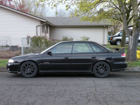 1998 Subaru Legacy - A black sedan is parked on the side of the road in front of a house.